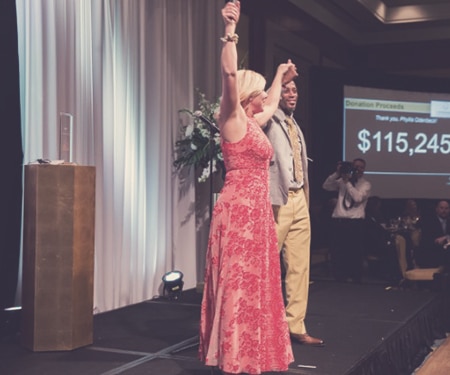 A Woman with her hands in the air celebrating at an event that achieved its fundraising goal by using mobile bidding